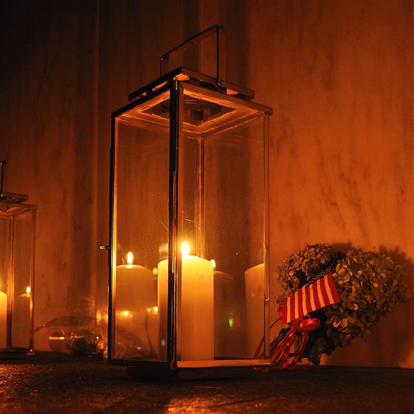 A candle light at night with flowers and an American flag behind it