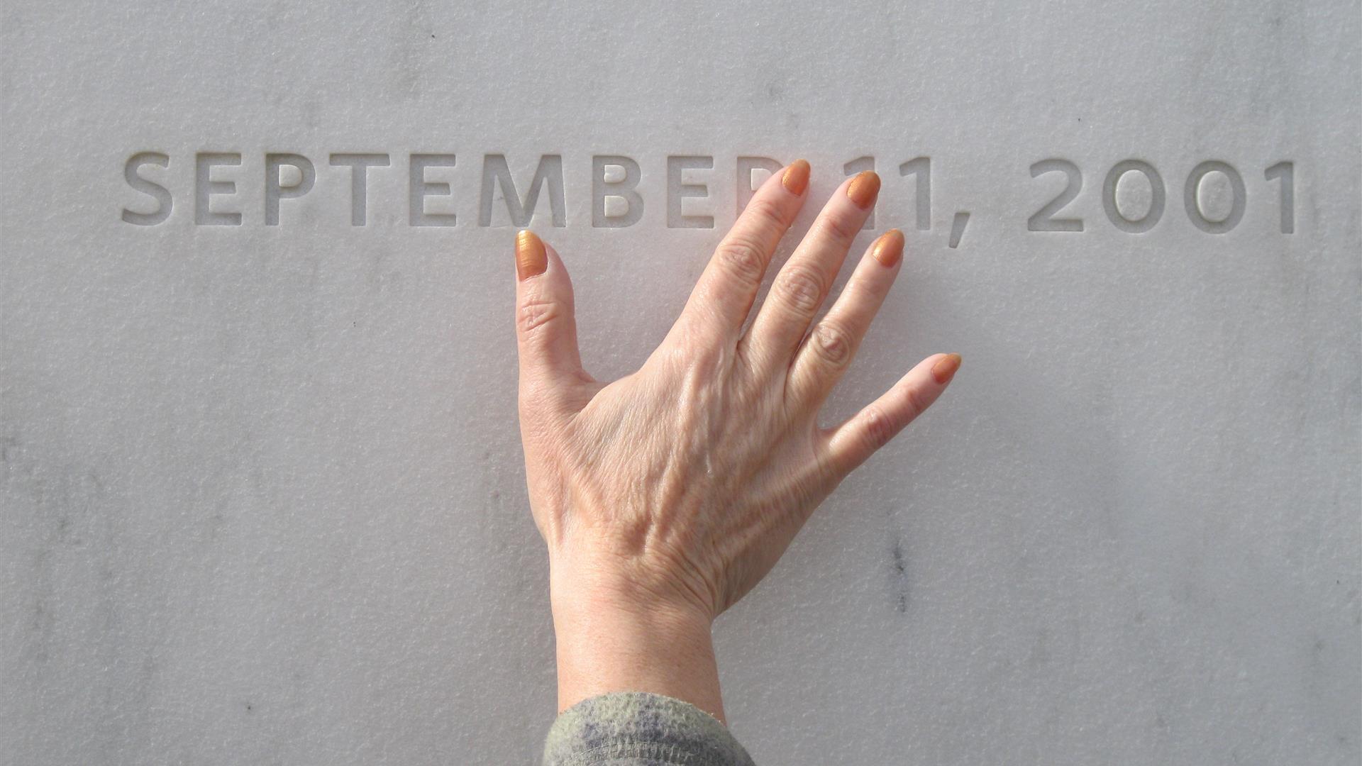 A hand on the memorial wall over the date September 11, 2001