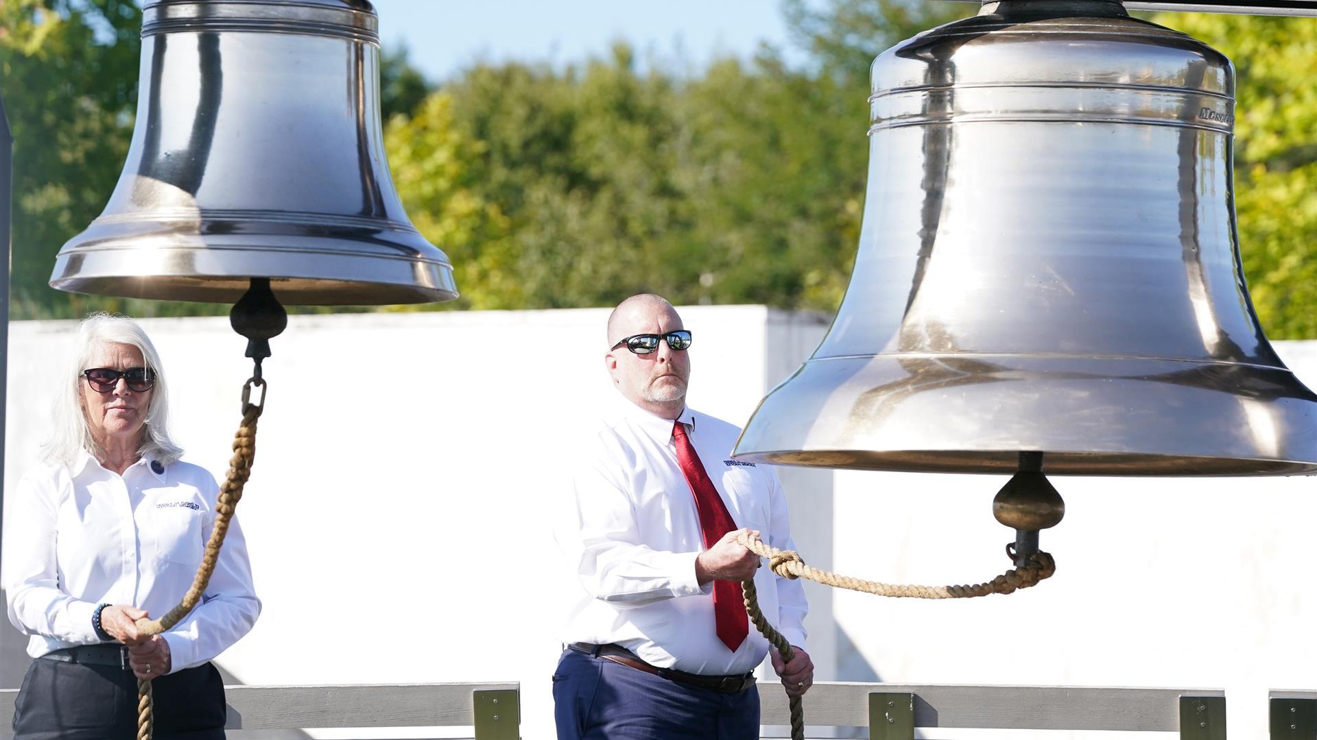 two people wearing sunglasses ringing two large silver bells