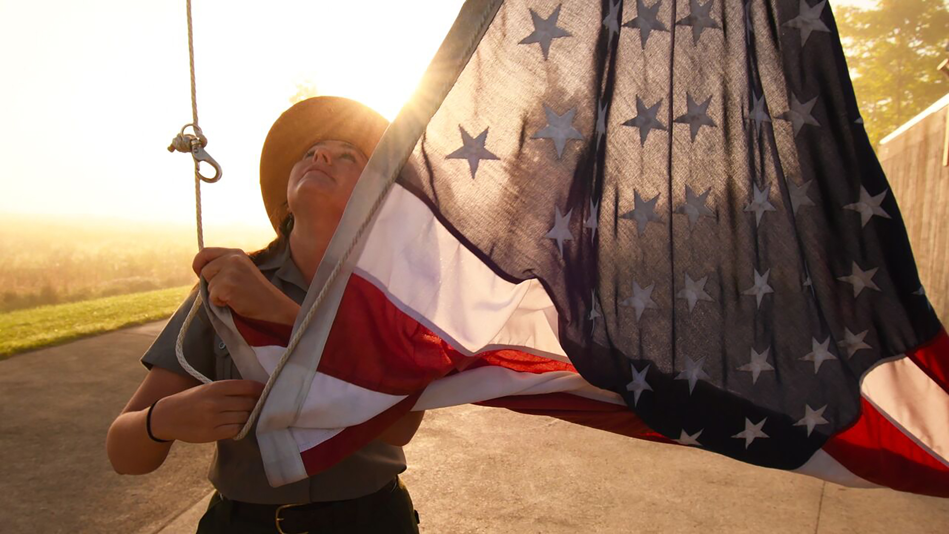 A woman looking up raising an American Flag on a pole