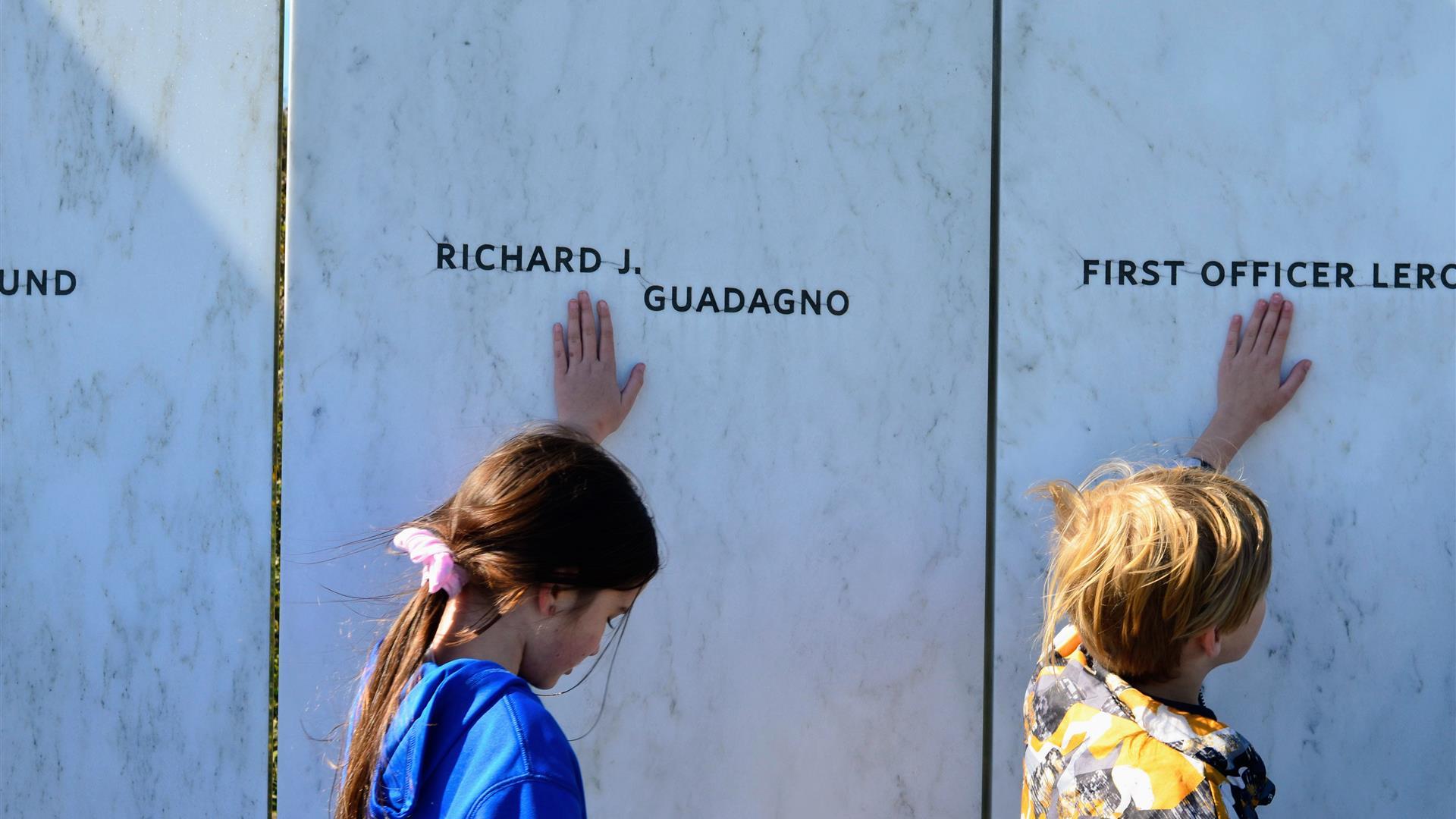 students touching a white wall with engraved names