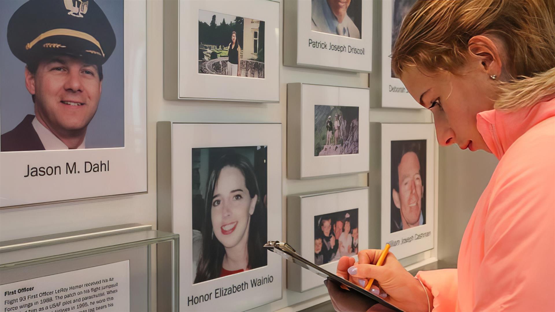 A woman writing on a clipboard in front of pictures of people