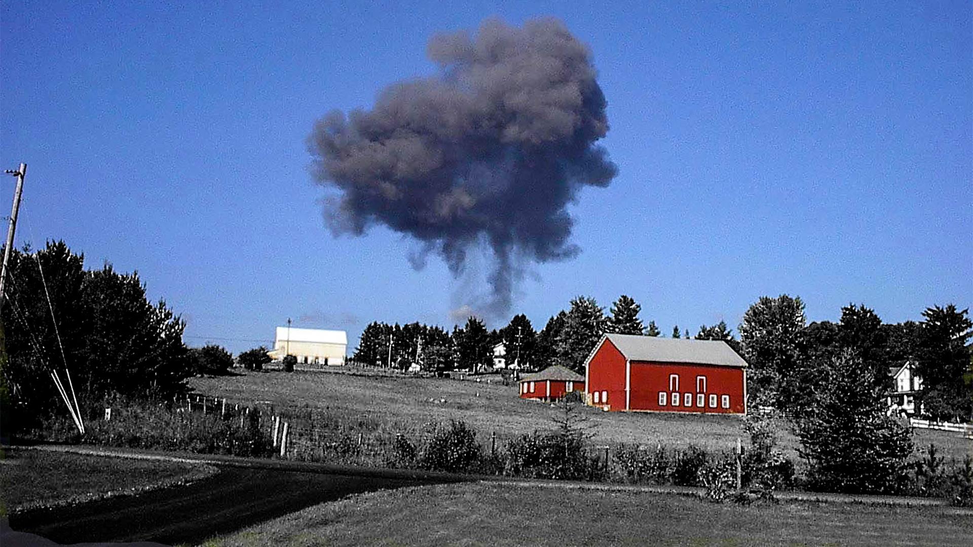 Red barn with smoke plume in blue sky.